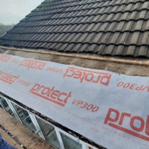 A close-up photograph of a roofing project showing the installation of 'protect VP300' breathable underlay beneath dark roof tiles in St Helens
